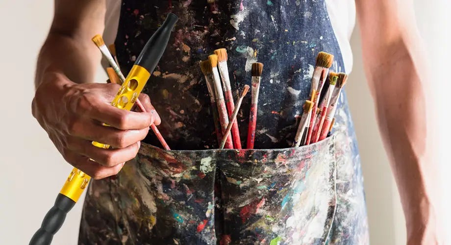 Artist with an apron covered in paint with paintbrushes in pockets holding a Shisha House Galaxy hookah hose